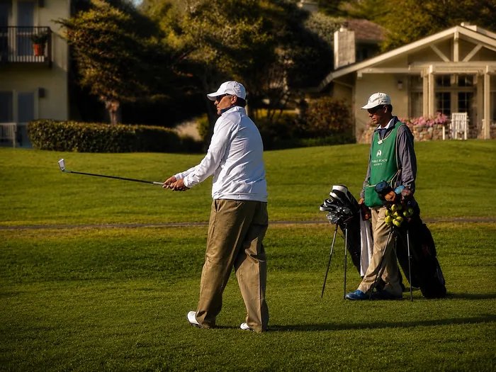 Hunt finishing a golf swing on the fairway at Pebble Beach in warm evening light, his caddie waiting with the bag beside him.